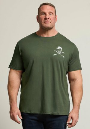 Mann mit kurzen Haaren, der ein olivgrünes T-Shirt mit einem weißen Totenkopf und gekreuzten Knochen auf der Brust trägt.