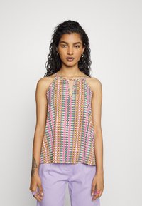 Top de halter multicolorido com um padrão geométrico, apresentando uma abertura em forma de olho de fechadura, feito de tecido leve, combinado com calças de lavanda.