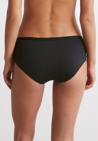 Zwarte bikini onderkant met een gladde, matte afwerking. Heeft een low-rise tailleband en naadloze randen voor comfort en minimale zichtbaarheid.