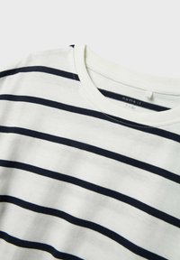 Witte katoenen t-shirt met marineblauwe horizontale strepen, voorzien van een ronde halslijn en zachte textuur. Etiket zichtbaar aan de binnenkant van de hals.