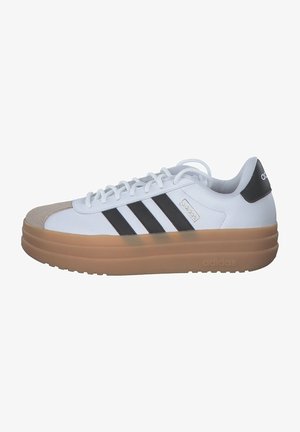 Zapatilla blanca con puntera gris y tres bandas negras. Presenta una suela gruesa y translúcida de goma. Marca en el lateral y en el talón en negro.