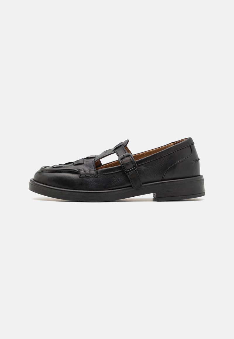 Chaussure Mary Jane en cuir noir avec bride à boucle, bout fermé orné d'un motif découpé, et petit talon carré, vue de profil sur fond blanc.