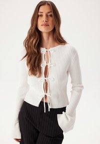 Biały sweter z prążkowanym splotem z głębokim dekoltem w kształcie litery V i wiązaniami, długimi rękawami z rozszerzanymi mankietami oraz dopasowanym krojem.