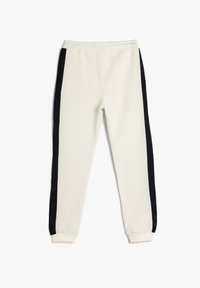 Cremefarvede sweatpants med sorte sidestriber, elastisk talje og tapered manchetter. Blød tekstur, afslappet design velegnet til afslappet brug.