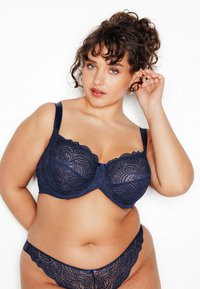 Reggiseno in pizzo blu navy con bordi smerlati, supporto con ferretto e spalline regolabili, abbinato a slip in pizzo coordinati con un motivo simile.