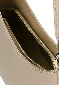 Intérieur d'un sac à main en cuir beige, comportant deux compartiments zippés avec des détails de fermeture éclair dorés et une texture lisse. Aucune autre caractéristique visible.