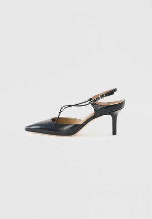 Sort læder slingback højhælet sko med spids tå og tynd T-rem, sat mod en enkel lys baggrund.