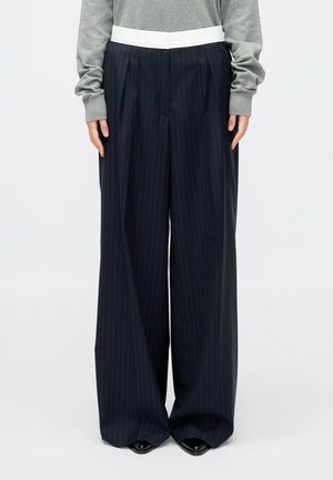 Ναυτικές παντελόνες με ρίγες και φαρδιά γραμμή, με λευκή ζώνη, που διαθέτουν πιέτες και λεία υφή, συνδυασμένες με γκρι μπλουζάκι μακρύ μανίκι.