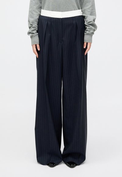 Navy pinstriped wide-leg trousers with a white waistband, featuring pleats and a smooth texture, paired with a gray long-sleeve top.