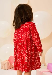 Rode lange mouwen jurk met een speelse witte feestelijke print, waaronder de Kerstman, peperkoekmannetjes en cadeaus. Elastische taille, van katoen.