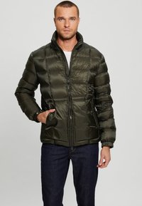Green puffer jacket with quilted design, high collar, front zipper, and side pockets. Made of shiny, smooth material.