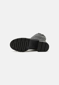 Botas de goma negras con suela texturizada, que presentan un diseño acanalado y un talón reforzado para mejorar el agarre y la estabilidad.