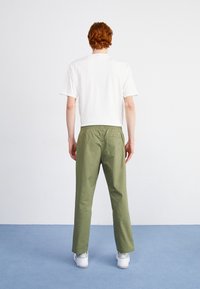 Zielone bawełniane spodnie o luźnym kroju, z elastycznym pasem, tylną kieszenią, w połączeniu z prostą białą koszulką i białymi trampkami.