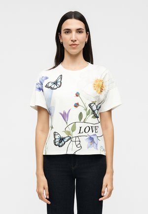 Egyenes sötét hajú nő, aki fehér pólót visel, melyen kék pillangók, színes virágok és a „LOVE” szó van nyomtatva.