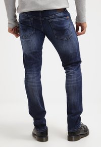 Mörkblå denimjeans med slim fit, med medelhög midja, två bakfickor med sömdetaljer och en slät yta.