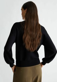Pullover nero lavorato a maglia con vestibilità rilassata, maniche a palloncino e polsini a coste, abbinato a pantaloni verde oliva con tasca posteriore.
