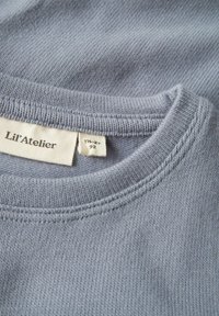 Hellblaues Strick-Sweatshirt mit rundem Ausschnitt, ausgestattet mit gerippten Bündchen und einem eingenähten Etikett, das Größen- und Markendetails anzeigt.