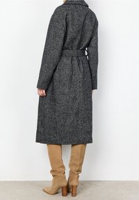 Szary płaszcz w jodełkę z paskiem w talii, długimi rękawami i średniej długości krojem, w zestawieniu z beżowymi kowbojkami do kolan o gładkiej fakturze.