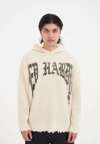 Cremfarbener Rippen-Hoodie mit großem schwarz bedrucktem Textdesign. Besitzt eine entspannte Passform, eine übergroße Silhouette und einen fransigen Saum.