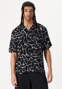 Camicia a maniche corte con bottoni di colore nero, con un motivo astratto bianco a contrasto, caratterizzata da una vestibilità rilassata e una texture di tessuto morbido.