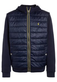 Mörkblå zip-up hoodie med en quiltad nylonfront, stickade ärmar och en gul dragkedja. Har en liten gul logotyp på bröstet.