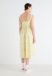 Žlté kvetinové midi šaty s priliehajúcim korzetom, volánovými ramienkami a stiahnutým pásom, skombinované s bielymi teniskami s ružovými akcentami.