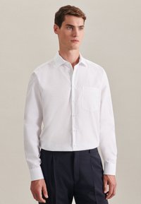 Witte lange mouwen shirt met een klassieke kraag, voorzak en knopenlijst; gecombineerd met marineblauwe broek, gladde stoftextuur.