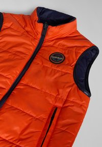 Gilet arancione con dettagli blu navy, frontalmente con zip e due tasche laterali. Presenta un design trapuntato e un'etichetta circolare sul petto.