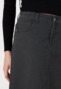 Črna denim krilo s sprednjim razporkom, z pasom, zankami za pas in stranskimi žepi. Gladka tekstura z diskretnimi šivi.