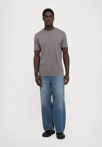 Grå kortermet t-skjorte med rund hals, kombinert med løse lyseblå denimjeans og svarte sko. Enkelt design, ingen mønstre.