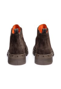 Botas de tobillo de ante marrón con una suela de goma oscura acolchada. El interior presenta un forro naranja brillante, con una pequeña lengüeta en la parte posterior.