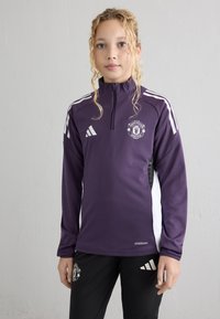 Purple athletic jacket with a quarter-zip, white accents, and Manchester United logo. Paired with black pants featuring a logo and stripes.