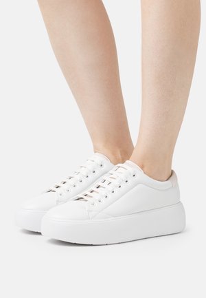 Baskets blanches à plateforme avec une tige en cuir lisse, bout arrondi et design à lacets plats. Accents rose clair au niveau du talon.