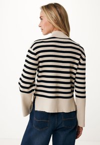 Maglione a righe in beige e nero, con maniche lunghe, texture a coste e orlo leggermente accorciato con spacchi laterali. Vestibilità casual.
