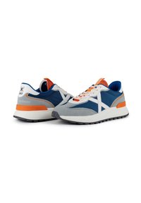 Baskets de sport avec un dessus en maille bleue et des accents en suède gris, logo blanc sur le côté, détails orange et une semelle intermédiaire blanche avec une semelle extérieure noire.
