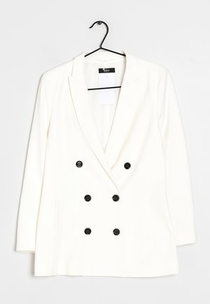 Blazer bianco doppiopetto con sei bottoni neri su appendiabiti nero su sfondo bianco.