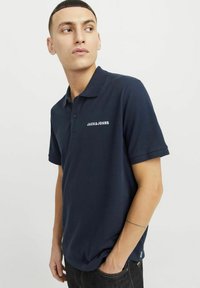 Marineblå polo skjorte lavet af bomuld med korte ærmer, der har en krave og hvid "JACK&JONES" logo på brystet. Struktureret stof med en glat overflade.