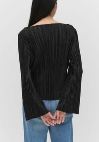 Sort plisseret top med vid halsudskæring og lange flagrende ærmer. Styling med lyseblå denim jeans. Struktureret stof med lodrette linjer.