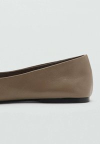 Zapato plano de cuero marrón con suela negra baja y tacón redondeado, visto de lado sobre un fondo liso.