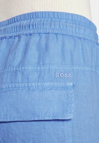 Short en tissu bleu clair avec taille élastique et une poche arrière brodée du mot BOSS en fil blanc.
