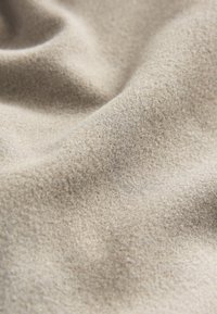 Bēšas krāsas audums ar mīkstu, strukturētu virsmu, kas izceļas ar gludu, viegli pūkainu izskatu un smalkām krāsu variācijām.