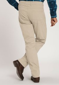 Chinos beige con corte recto, que cuentan con dos bolsillos traseros y detalles de costura sutiles. Combinados con zapatos marrón oscuro.