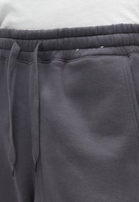 Pelēki treniņbikses ar elastīgu jostasvietu, ar auklu un mīkstu, teksturētu audumu komfortam.