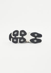 Sneakers with a textured black rubber outsole, featuring geometric patterns and a contrasting off-white midsole.