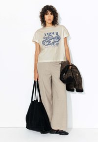 T-shirt en coton beige avec imprimé "AMOUR", pantalon large beige, sac cabas en suède noir, veste à motif léopard brun, et chaussures noires à enfiler.