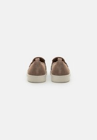 Chaussures slip-on en suede marron avec une semelle en caoutchouc crème et une languette à l'arrière, présentant une forme arrondie et un design minimaliste.