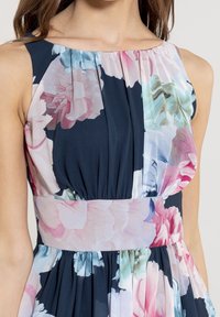 Robe florale avec une base navy, ornée d'imprimés de pivoine roses et bleus, un corsage plissé et une taille unie. Tissu léger.