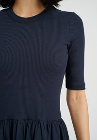 Marineblaue, gerippte Kurzarmkleid mit tailliertem Oberteil und fließendem, gerafftem Rock. Glatte Textur mit rundem Ausschnitt.