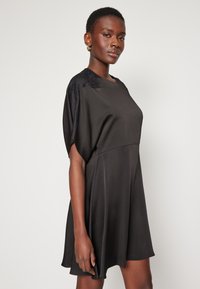 Μαύρο φόρεμα με χαλαρή γραμμή, κοντά ριχτά μανίκια με υφή, και απαλό ύφασμα που φτάνει πάνω από το γόνατο.