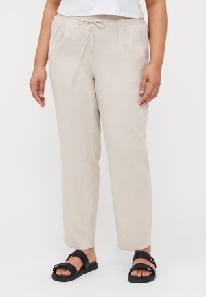 Beige Leinenhose mit elastischem Bund und Schnürdetail. Gerade Schnittform und zwei Fronttaschen. Getragen mit schwarzen Sandalen.
